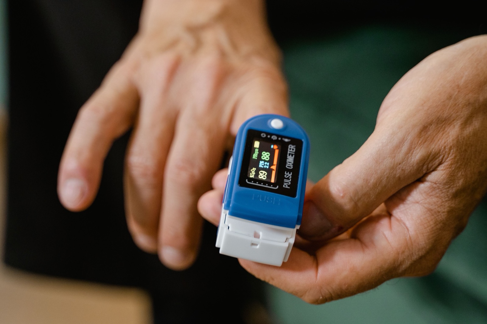 A pulse oximeter clipped to a finger, showing a live reading