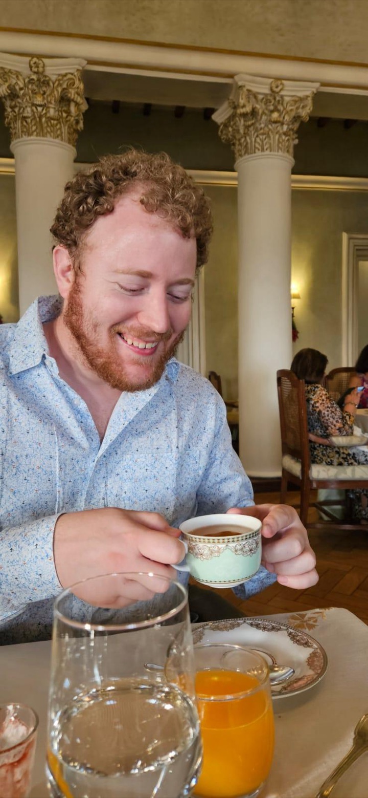 Steven smiling over a cup of coffee in a colonnaded dining room